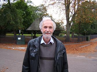 grey-haired man in a waxed jacket standing outside a park in autumn